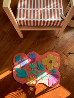 a pink rug with flowers and leaves on it next to a wooden chair in a room