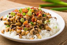 a white plate topped with rice and beans on top of a wooden table next to green onions