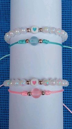 three bracelets with beads and hearts on them sitting on a white cylinder against a blue background