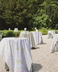 several tables covered with white tablecloths in front of trees