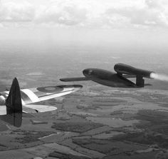 two planes flying side by side in the sky above land and trees, with one plane upside down