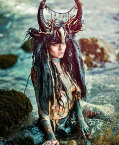 a woman with long hair and horns sitting in the water