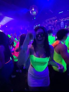 a woman in a white dress dancing at a party with other people and lights behind her