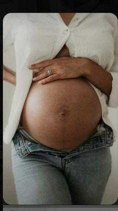 a pregnant woman's belly is shown with her hand on her stomach and the bottom half of her jeans