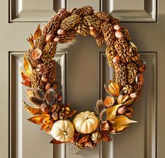 a wreath with pumpkins, leaves and acorns hanging on the front door