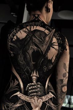 the back of a woman's body with tattoos on her arms and chest, holding a knife