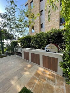 an outdoor bbq grill in the middle of a courtyard with trees and bushes surrounding it