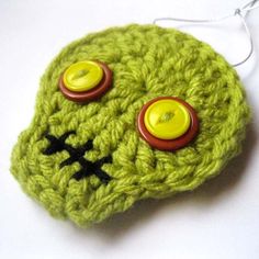 a green crocheted object with two yellow buttons on it's eyes and nose