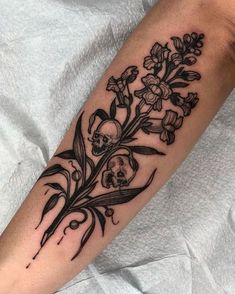 a skull and flowers tattoo on the left arm, with black ink overlays