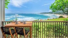 two chairs sitting on top of a wooden table next to an open window with the ocean in the background