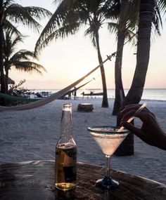 a person holding a drink in front of a glass on a table near the beach