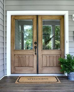 a welcome mat on the front door of a house with two double doors and potted plants