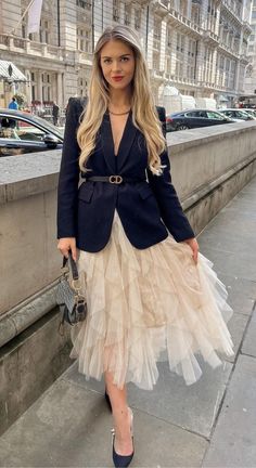 a woman in a dress and jacket is standing on the sidewalk