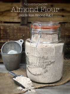 a jar filled with white flour next to a measuring cup and spoon on top of a burl