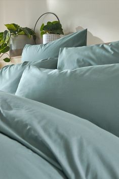 a bed with blue sheets and pillows next to a potted plant