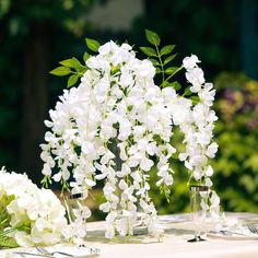 white flowers are arranged in vases on a table with silverware and napkins