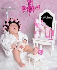 a baby in a bathrobe sitting next to a vanity with a mirror and hair dryer