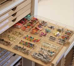 a drawer filled with lots of different types of buttons and pins on top of a wooden table