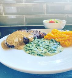 a white plate topped with meat and veggies next to a bowl of sauce