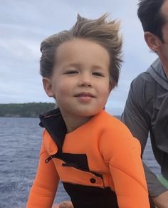 a young boy in an orange life jacket sitting next to his father on a boat