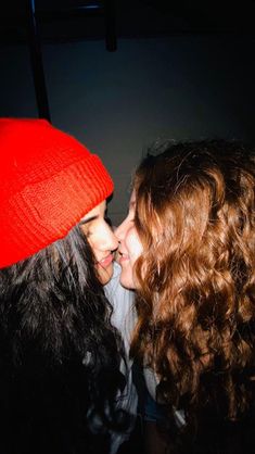 two women are kissing each other while wearing red beanies and black jackets in the dark