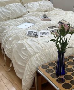 a bed with white comforter and flowers in a vase on the end table next to it