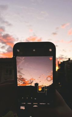 someone holding up their cell phone to take a photo with the sunset in the background