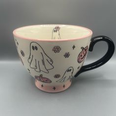 a black and white coffee cup with halloween ghostes on it's side, in front of a gray background