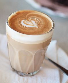 a close up of a cup of coffee on a table with a heart pattern in the foam