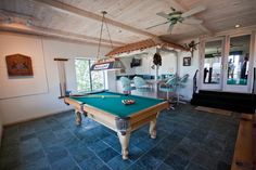 a pool table in the middle of a room with chairs around it and a fan hanging from the ceiling