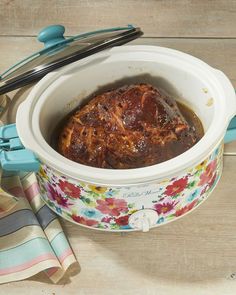 a slow cooker filled with food on top of a wooden table next to utensils