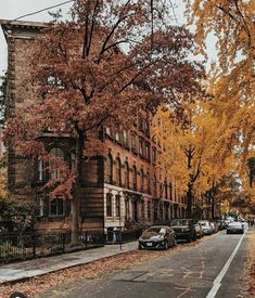 an old brick building on the corner of a street with parked cars and trees in autumn