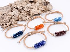 six bracelets with beaded beads and leather cord on a white surface next to a rock