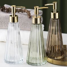 three glass soap dispensers sitting on top of a counter next to towels