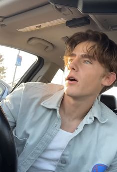 a young man sitting in the passenger seat of a car with his mouth open and tongue out