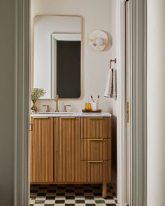 a bathroom with a checkered floor and wooden cabinetry, along with a mirror on the wall