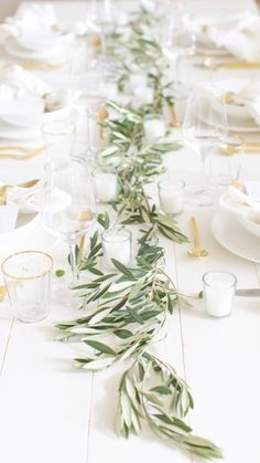 the table is set with white plates and silverware, greenery on each side