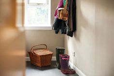 a coat rack with clothes hanging on it next to a basket and booties in front of a window