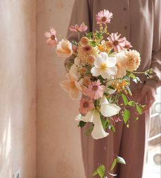 a person standing next to a vase with flowers in it and wearing a brown suit