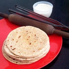 a red plate topped with three tortillas next to a knife and bowl of sour cream