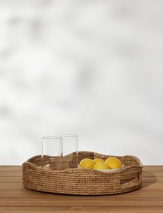 a wicker tray with lemons in it on a wooden table next to two glasses