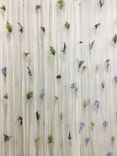 the wall is made up of flowers and grass on white sheer fabric, with small blue flowers growing from them