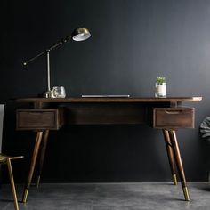 a wooden desk with two drawers and a lamp on the top, in front of a black wall