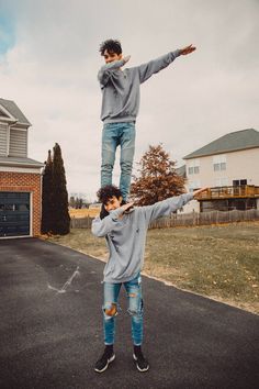 two young men standing on top of each other in the middle of a driveway with their arms outstretched