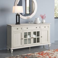 a white dresser with a mirror and vases on it in front of a blue wall