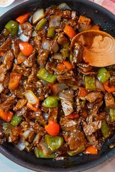 a wooden spoon in a skillet filled with beef and vegetables