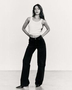 black and white photograph of a woman standing with her hands on her hips wearing high - waisted jeans