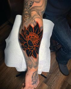 a man's arm with an orange and black flower tattoo on his left arm