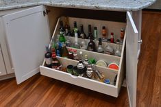 an open cabinet filled with liquor bottles and condiments on top of a wooden floor