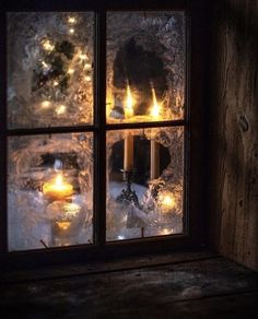 candles are lit in front of a window with frost on the windowsill and snow outside